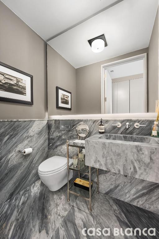 bathroom with toilet, a wainscoted wall, marble finish floor, and tile walls