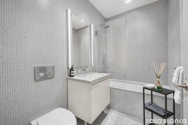 bathroom with toilet, a combined bath / shower with marble appearance, vanity, and tile walls