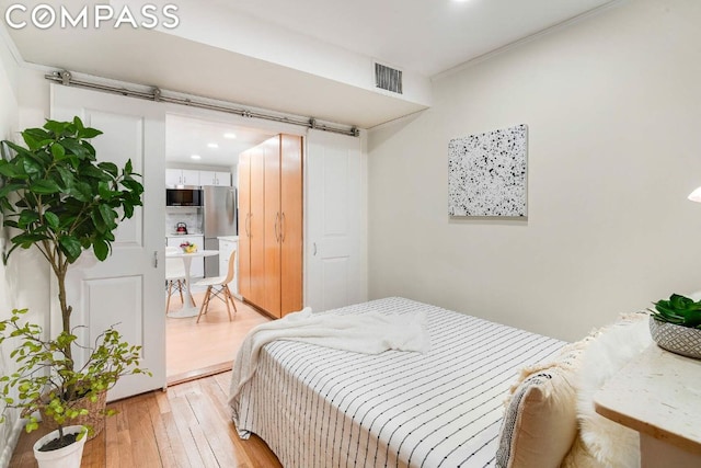 bedroom featuring light wood-type flooring, stainless steel refrigerator, and a barn door