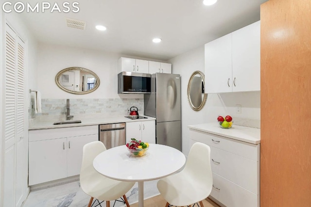 kitchen with tasteful backsplash, stainless steel appliances, sink, and white cabinets