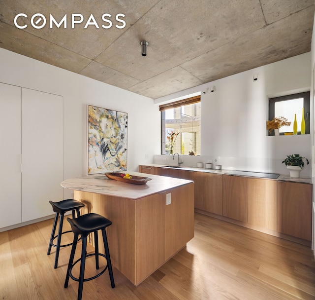 kitchen with light wood finished floors, brown cabinetry, modern cabinets, a kitchen breakfast bar, and a center island