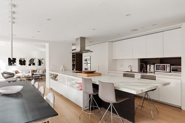 kitchen featuring white cabinetry, a breakfast bar area, island exhaust hood, light hardwood / wood-style floors, and light stone countertops