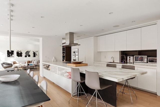 kitchen featuring a breakfast bar area, white cabinets, light wood finished floors, stainless steel microwave, and island exhaust hood