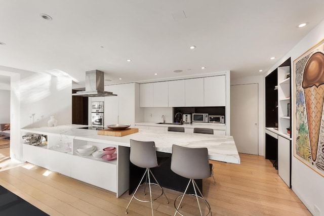 kitchen with a breakfast bar area, white cabinets, island exhaust hood, light hardwood / wood-style floors, and stainless steel appliances