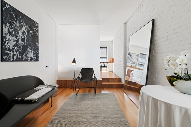 sitting room with brick wall and light hardwood / wood-style flooring