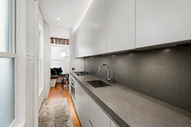 kitchen with sink, light wood-type flooring, stainless steel gas stovetop, decorative backsplash, and white cabinets