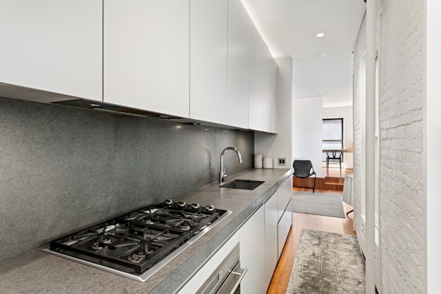 kitchen with sink, light hardwood / wood-style floors, white cabinets, oven, and stainless steel gas stovetop