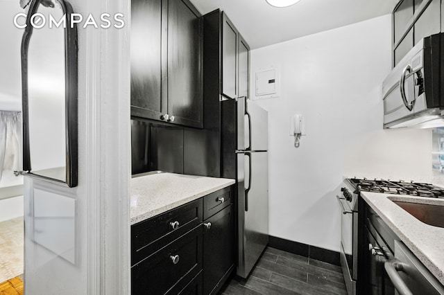 kitchen featuring baseboards, light stone countertops, stainless steel appliances, dark cabinetry, and wood finish floors