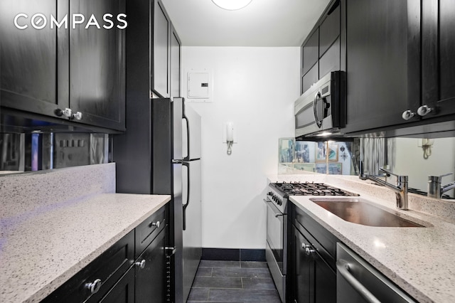 kitchen featuring a sink, appliances with stainless steel finishes, dark cabinets, baseboards, and light stone countertops