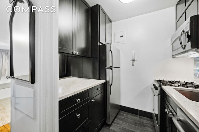 kitchen featuring stainless steel appliances, dark cabinets, and light stone counters