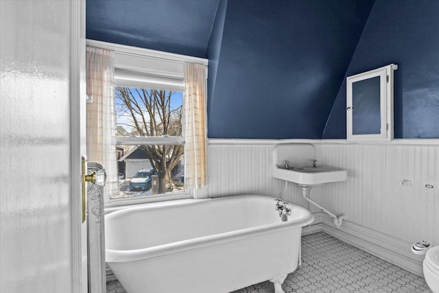 full bathroom with lofted ceiling, tile patterned flooring, a freestanding bath, and wainscoting