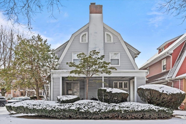 snow covered facade featuring a chimney and a gambrel roof