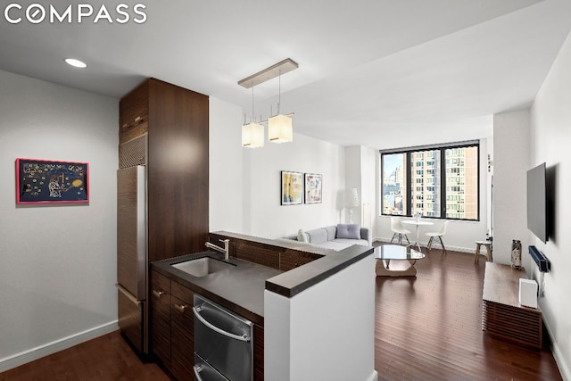 kitchen with built in fridge, sink, hanging light fixtures, kitchen peninsula, and dark brown cabinets