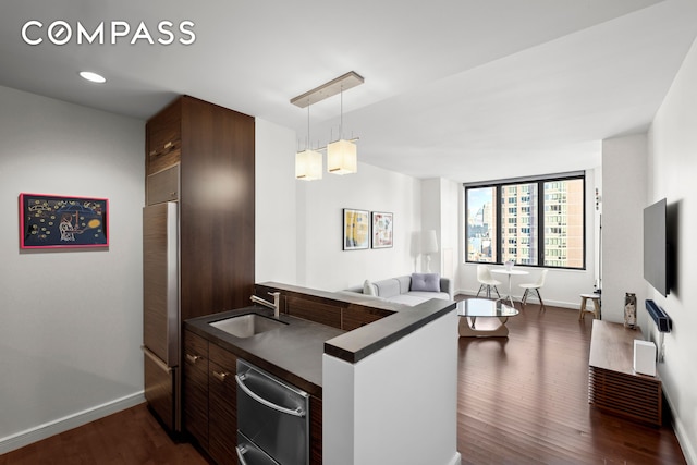 kitchen featuring a peninsula, a sink, dark countertops, dark wood finished floors, and decorative light fixtures