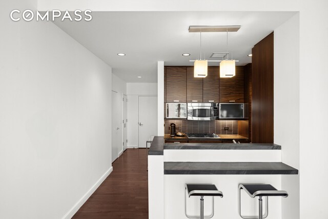 kitchen featuring a breakfast bar, dark countertops, stainless steel microwave, and backsplash