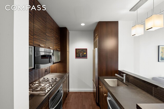 kitchen with a sink, appliances with stainless steel finishes, tasteful backsplash, dark countertops, and dark wood finished floors