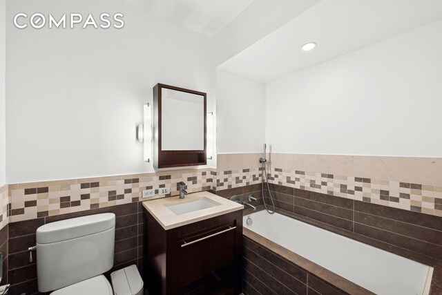 bathroom with wainscoting, toilet, a garden tub, vanity, and tile walls