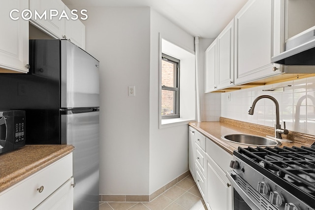 kitchen featuring stainless steel appliances, decorative backsplash, light tile patterned flooring, a sink, and white cabinetry