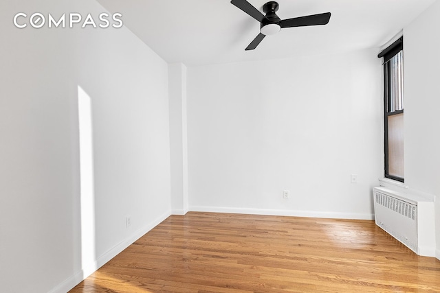 spare room featuring baseboards, ceiling fan, light wood-style floors, and radiator