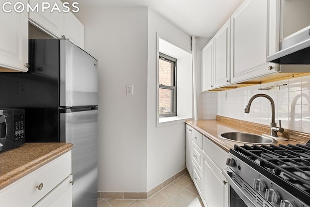 kitchen featuring sink, white cabinetry, light tile patterned floors, appliances with stainless steel finishes, and backsplash