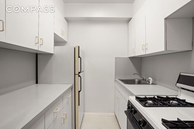 kitchen with gas range, white fridge, sink, and white cabinets