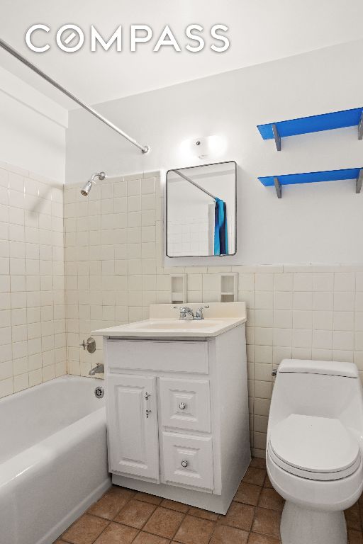 full bathroom featuring tile walls, tile patterned flooring, vanity, tiled shower / bath combo, and toilet