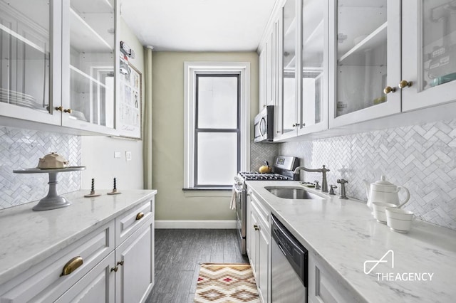 kitchen featuring glass insert cabinets, a sink, appliances with stainless steel finishes, and light stone counters