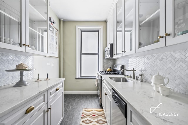 kitchen featuring baseboards, dark wood finished floors, appliances with stainless steel finishes, white cabinetry, and a sink