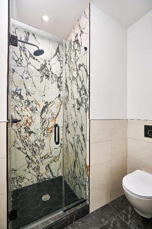 bathroom with tile walls, an enclosed shower, and toilet