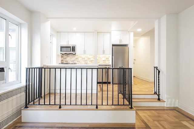 kitchen featuring plenty of natural light, white cabinets, stainless steel appliances, and radiator heating unit