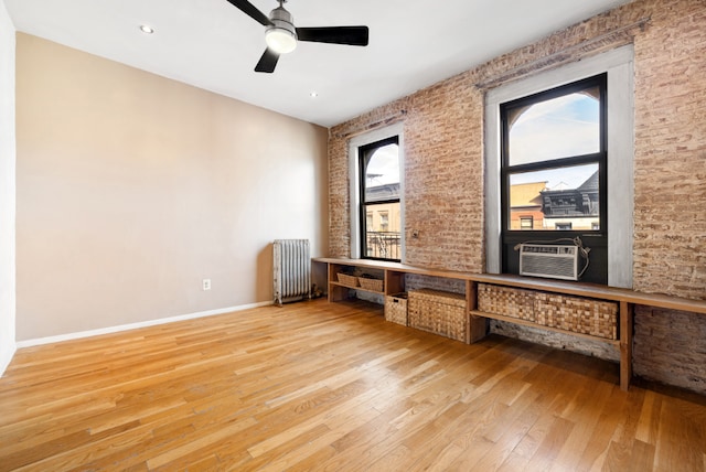 interior space with ceiling fan, cooling unit, radiator heating unit, brick wall, and light wood-type flooring