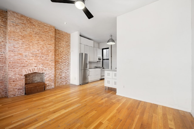 unfurnished living room featuring brick wall, ceiling fan, and light wood finished floors