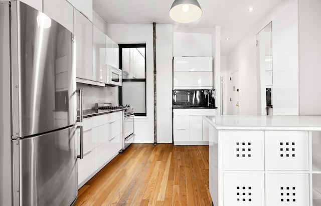 kitchen with white microwave, white cabinetry, freestanding refrigerator, gas range oven, and modern cabinets