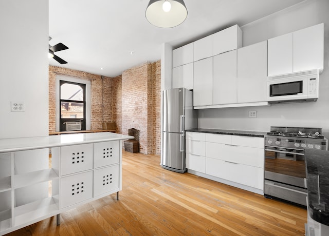 kitchen with stainless steel appliances, white cabinetry, light wood-style floors, and brick wall