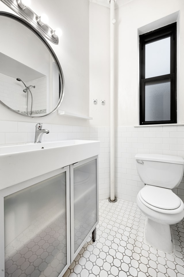 bathroom featuring toilet, a wainscoted wall, vanity, and tile walls