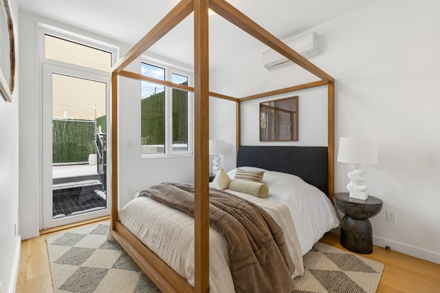 bedroom featuring light hardwood / wood-style flooring, a wall unit AC, and access to outside