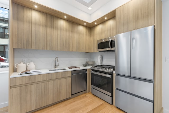 kitchen featuring light brown cabinetry, tasteful backsplash, sink, stainless steel appliances, and light hardwood / wood-style flooring