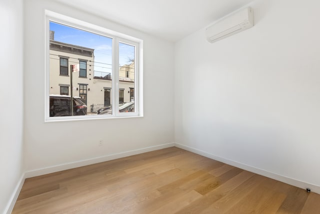 spare room featuring light wood-style flooring, baseboards, and a wall mounted AC