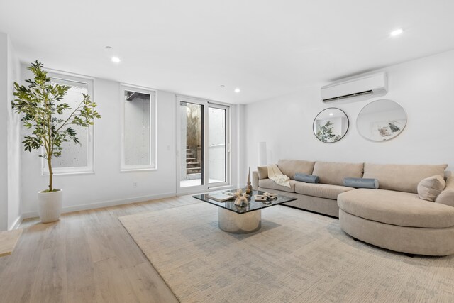 living room featuring recessed lighting, baseboards, a wall unit AC, and light wood finished floors