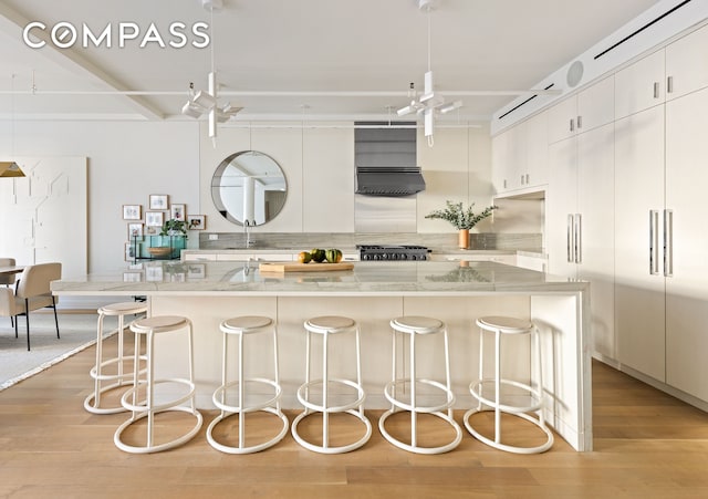 kitchen with tasteful backsplash, a breakfast bar area, light wood-type flooring, and under cabinet range hood