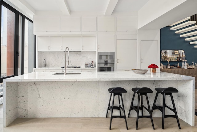 kitchen with a spacious island, light wood-style flooring, stainless steel double oven, white cabinets, and beamed ceiling