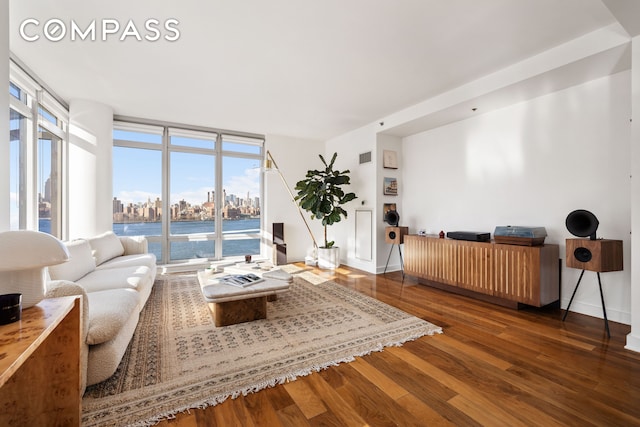 living area with visible vents, a view of city, wood finished floors, floor to ceiling windows, and baseboards