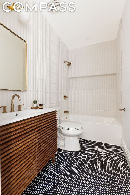 full bathroom featuring tiled shower / bath, vanity, toilet, and tile walls