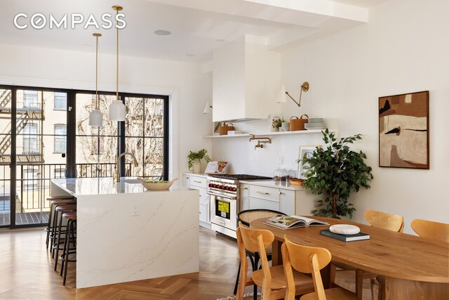 kitchen featuring sink, stainless steel stove, hanging light fixtures, dark parquet floors, and white cabinets