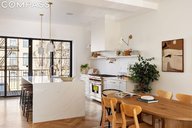 kitchen featuring dark parquet flooring, sink, hanging light fixtures, high end stove, and white cabinets