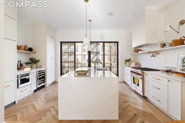 kitchen with pendant lighting, stainless steel appliances, wine cooler, light stone countertops, and white cabinets