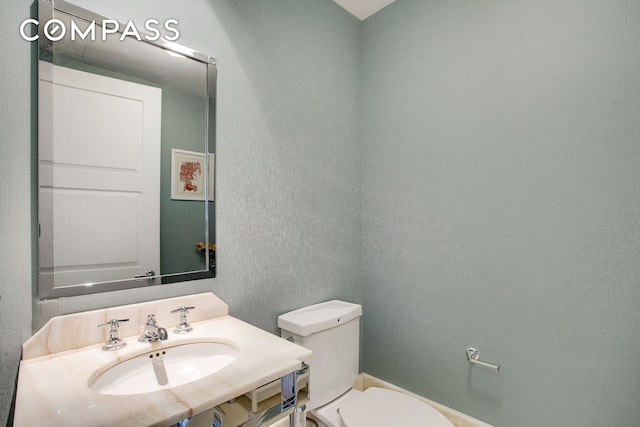 bathroom featuring a sink, toilet, and a textured wall