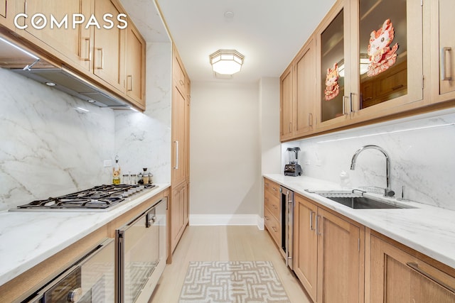 kitchen with beverage cooler, light stone countertops, a sink, stainless steel gas stovetop, and glass insert cabinets