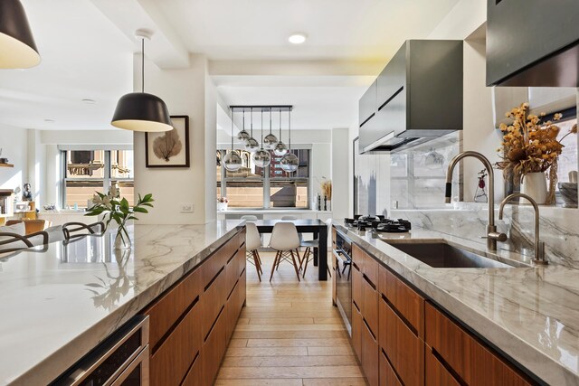 kitchen featuring sink, oven, hanging light fixtures, light stone counters, and light hardwood / wood-style floors