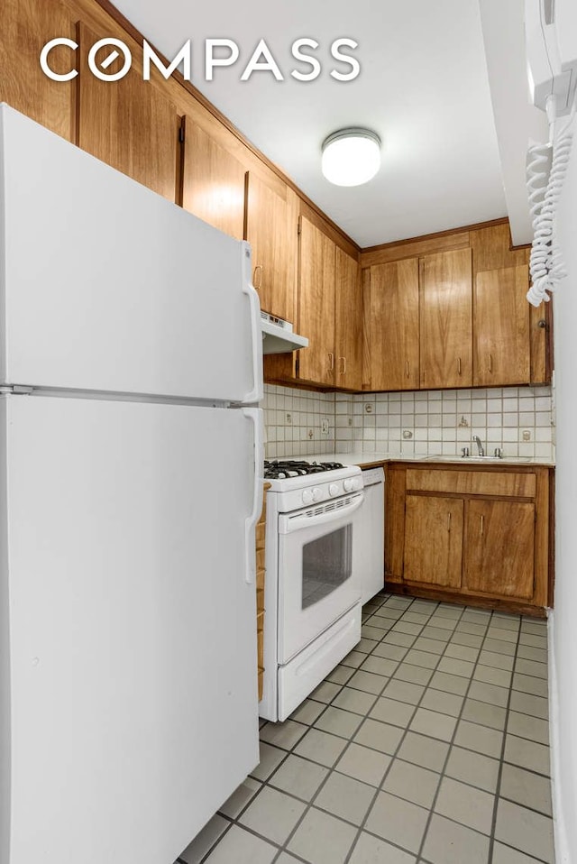 kitchen with white appliances, under cabinet range hood, decorative backsplash, light countertops, and brown cabinets